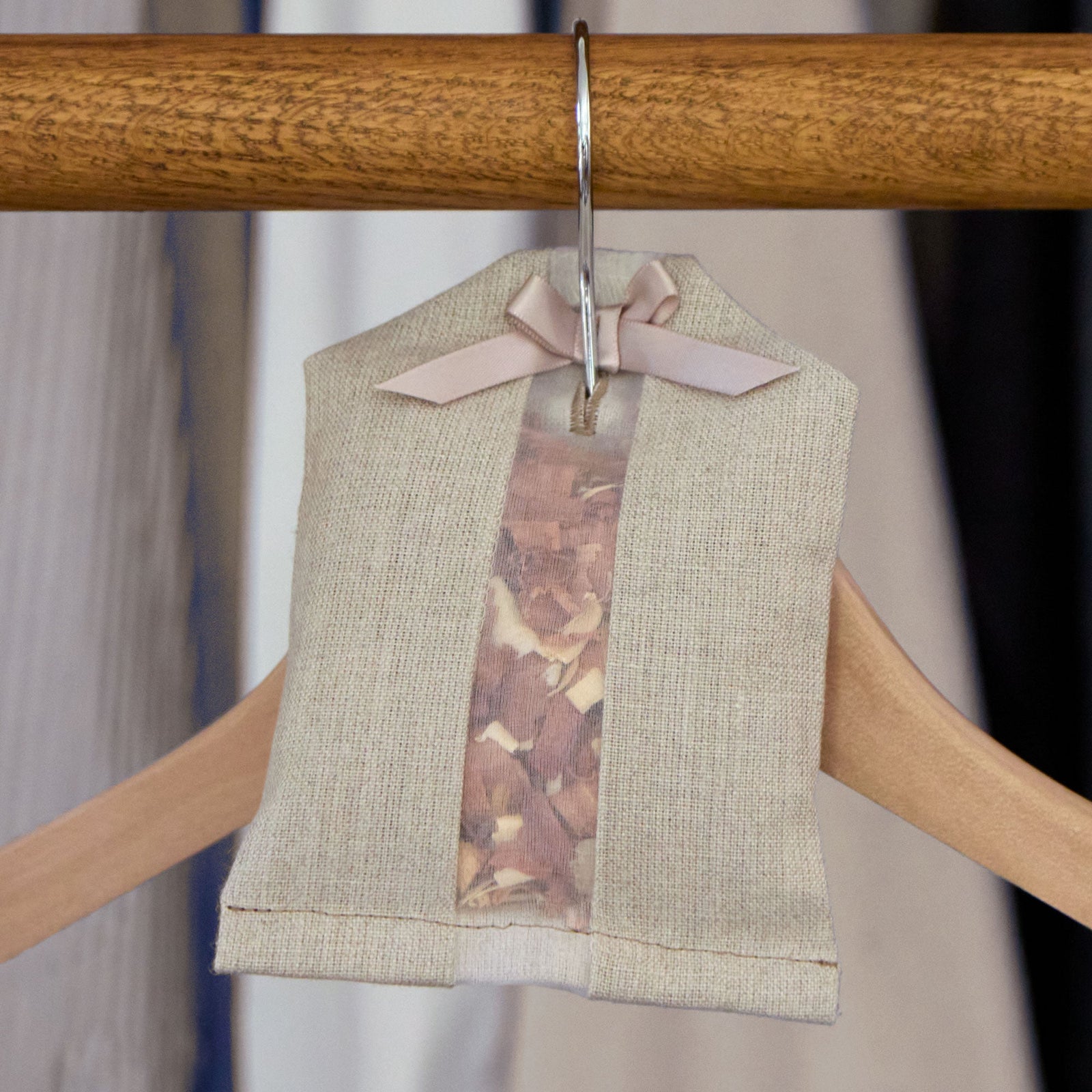 A fabric sachet filled with wood chips hangs on a wooden hanger in a closet, decorated with a ribbon bow at the top.