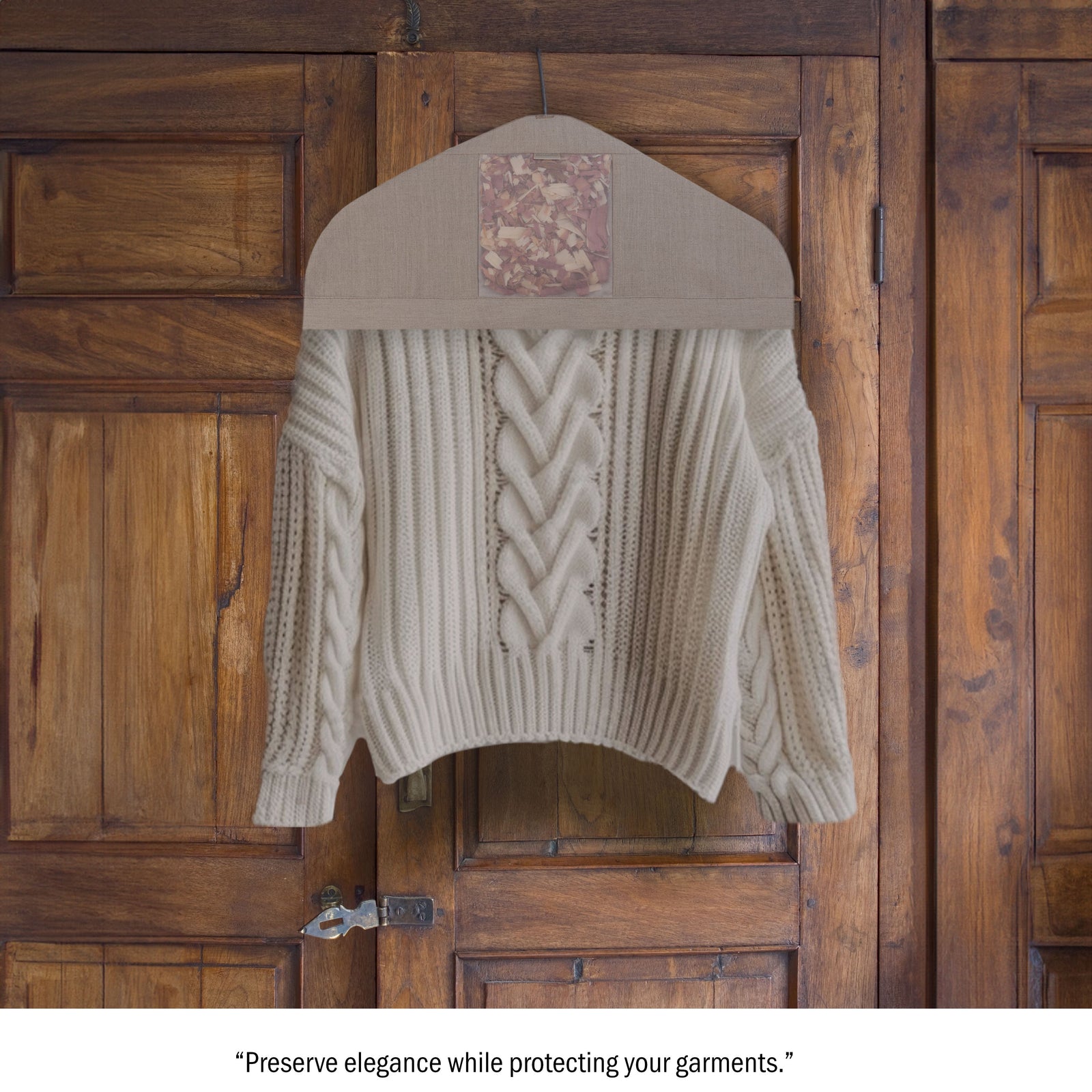A beige sweater is hanging in a fabric cover on a wooden closet door with a vintage-style latch. The cover has a patterned patch at the top.