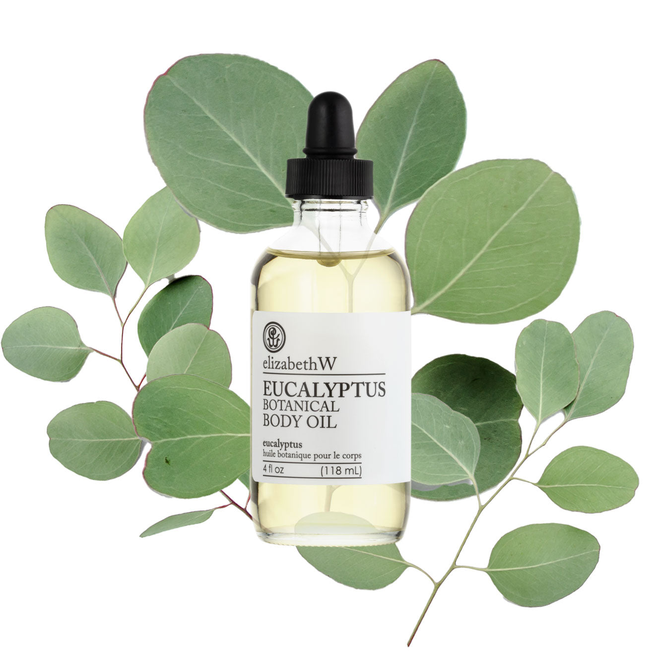 A glass dropper bottle of elizabethW Eucalyptus Botanical Body Oil is surrounded by fresh eucalyptus leaves on a white background.