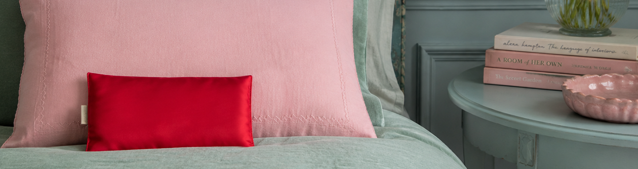 A rectangular black pillow with vibrant pink, red, and orange floral patterns, surrounded by matching painted flowers on a white background.
