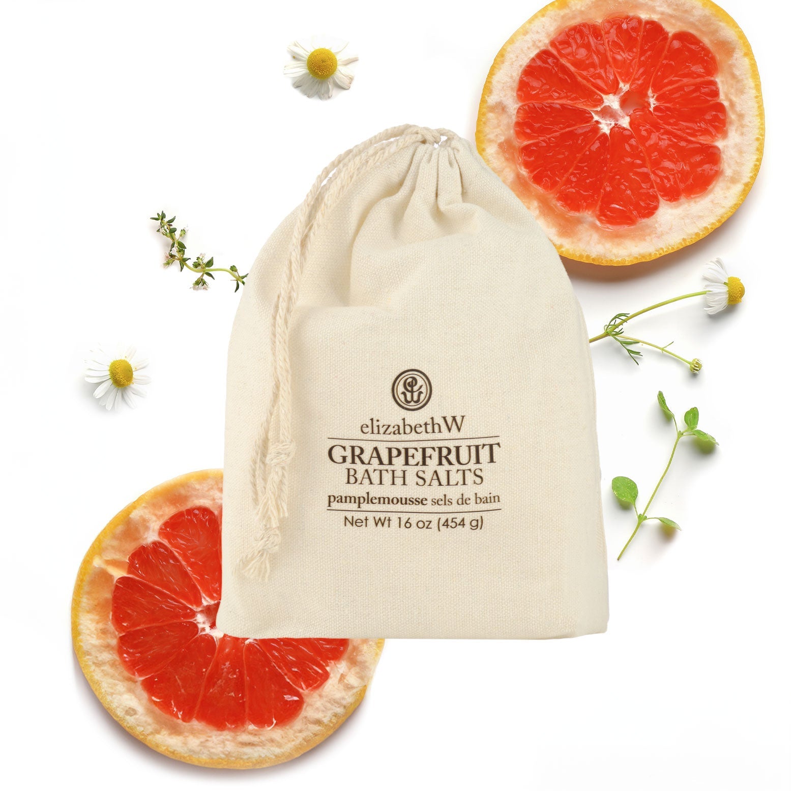 A cloth bag labeled "elizabethW Grapefruit Bath Salts" sits on a white background, surrounded by grapefruit slices and small chamomile flowers.