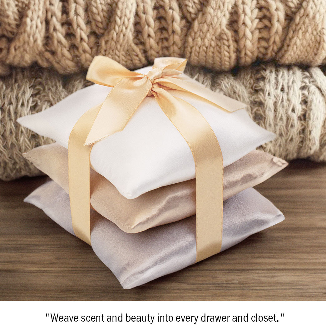 Stack of cozy, folded, beige knitted sweaters beside three small, white cushions tied together with a satin ribbon. The sweaters feature different knit patterns, adding texture and warmth to the arrangement.