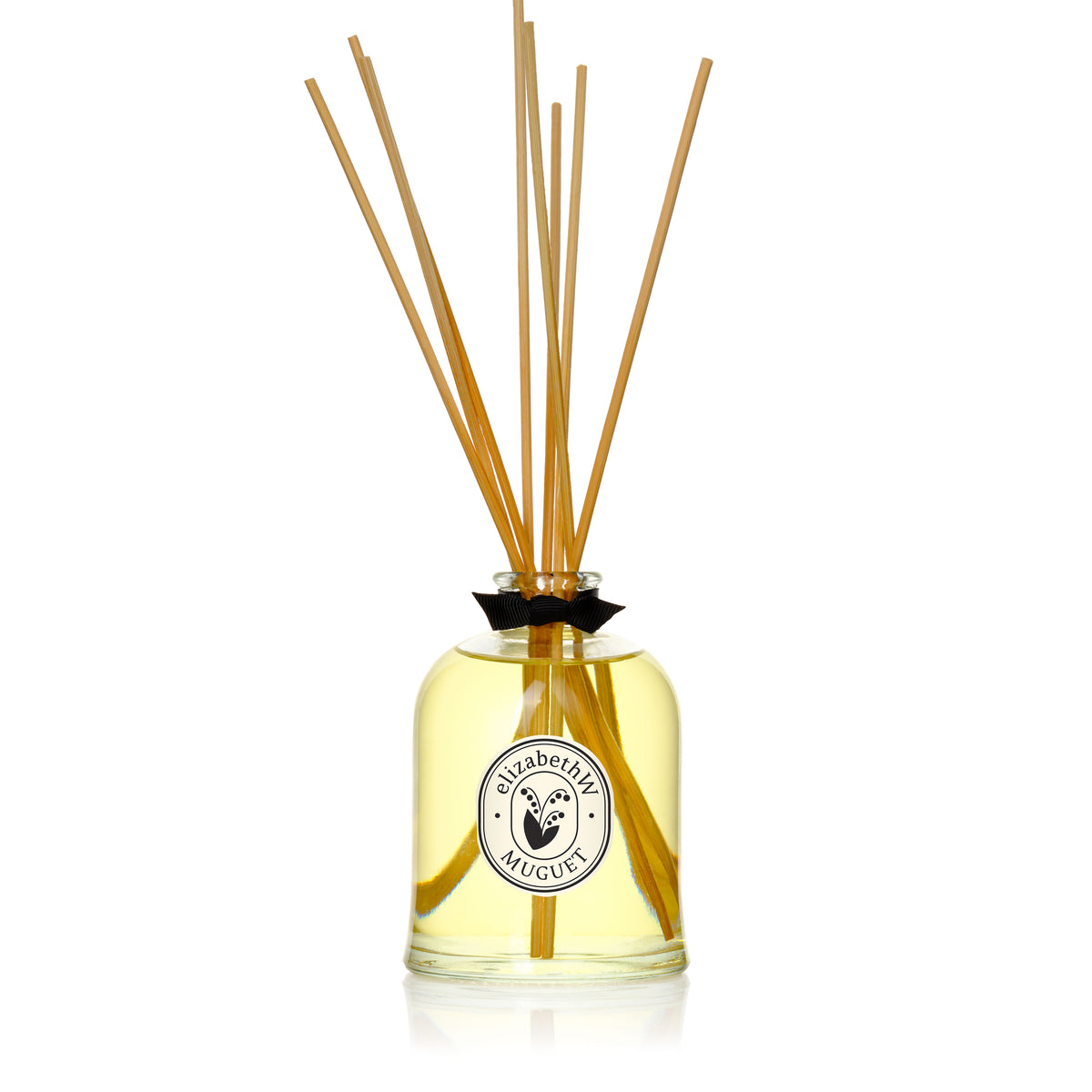 The elizabethW Muguet — Diffuser features an eco-friendly glass bottle of yellow liquid, long wooden reeds, and a round label. Enjoy a stylish, low-VOC home fragrance that lasts and enhances your space.