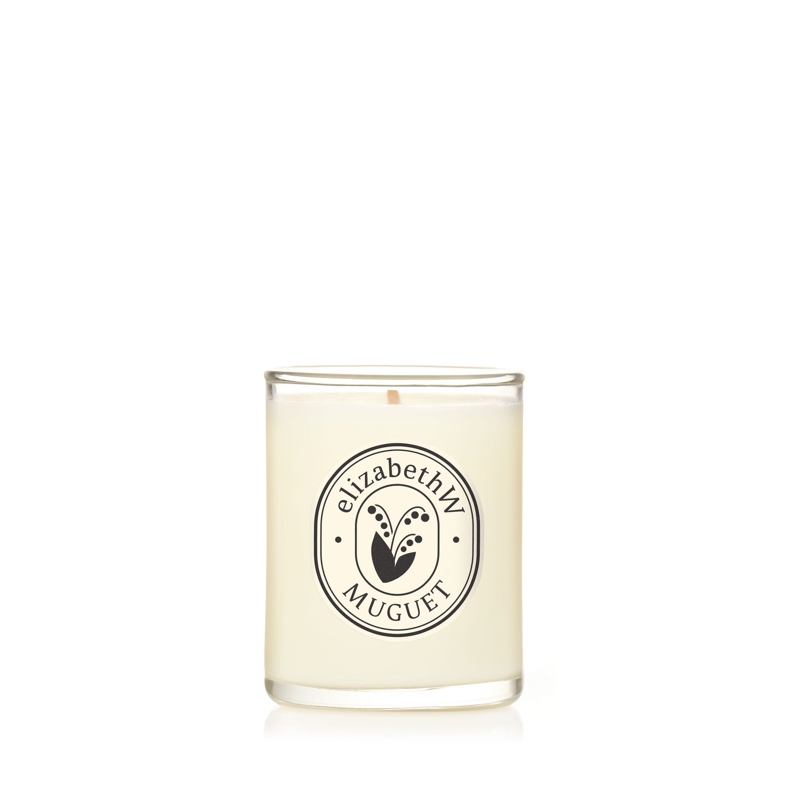 The elizabethW Muguet — Petite Perfume Candle is a hand-poured white scented candle in a clear glass holder with a black and white "elizabethW Muguet" label and lily of the valley design, made from renewable soy wax.
