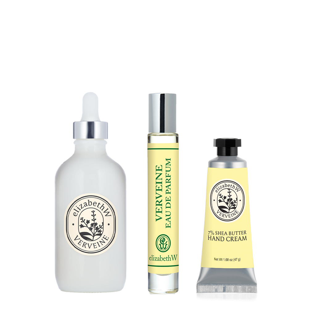 The elizabethW Verveine Bundle, featuring a white dropper bottle of body oil, a yellow-labeled perfume rollerball, and a silver tube of citrus hand cream with a matching yellow label, stands upright on a white background.