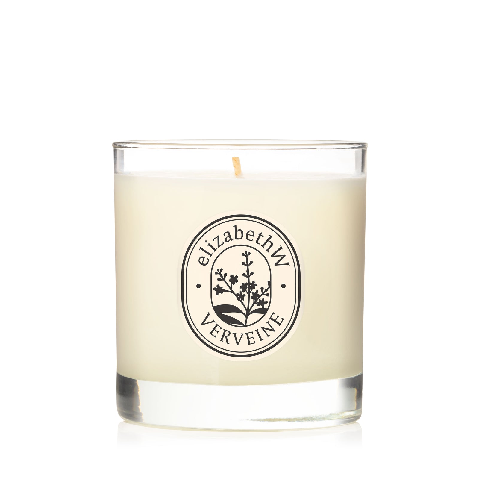 The elizabethW Verveine — Perfume Candle is a hand-poured soy wax candle in a clear glass jar, featuring a black botanical design and label. This scented candle has a single, unlit wick.