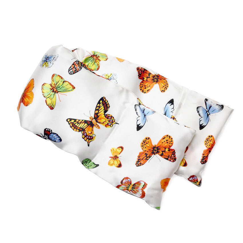 Neatly arranged against a plain white background, the elizabethW  Butterfly Hot/Cold Flaxseed Pack is covered in a silk casing adorned with vibrant butterfly prints in orange, yellow, blue, and multicolored designs, and can be used as a heat pad or cold compress.