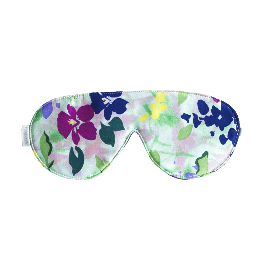 The Impressions Sleep Mask by elizabethW is a luxurious silk sleep mask adorned with a vibrant floral pattern in shades of purple, green, yellow, and blue. It includes adjustable strap to ensure it secures comfortably around your head for a restful sleep.