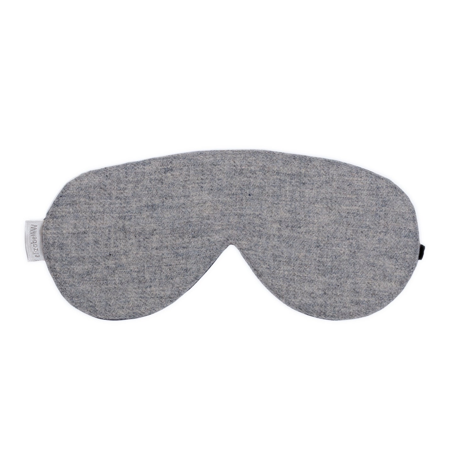 The Wool Heather Gray Sleep Mask by elizabethW is a light gray colored sleep mask with a sleek, curved design. It features a silk underside for enhanced comfort, along with an adjustable velvet strap to ensure it secures comfortably around your head for a restful sleep. 